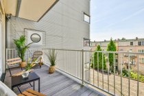 Amplia terraza de madera con cómodas sillas y plantas en maceta en la moderna casa de apartamentos - foto de stock