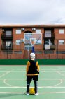Arrière vue sportif anonyme en vêtements de sport debout sur le terrain de sport public avec balle jaune et panier de basket-ball pendant le match dans la rue — Photo de stock