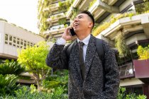 Jovem empreendedor masculino étnico alegre com gravata olhando para a frente enquanto fala no celular na cidade — Fotografia de Stock
