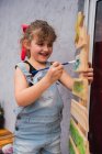 Menina focada em denim pintura geral com pincel na árvore de Natal decorada na sala de luz durante a preparação de férias em casa — Fotografia de Stock