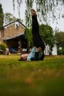Вид збоку тіла босоніж дівчина робить Арду Сараванасану позу на трав'янистому газоні на подвір'ї біля будівлі в сільській місцевості — стокове фото