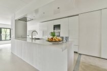 Contemporary kitchen interior with stainless steel tap against fresh fruits on plate in light house — Stock Photo