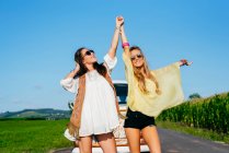 Duas lindas e felizes garotas caucasianas vestidas com roupas de verão em pé na estrada fora de uma van — Fotografia de Stock