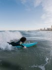 Вид сбоку на молодую женщину-серфингистку в гидрокостюме, лежащую на волнах моря и наслаждающуюся летним днем — стоковое фото