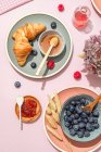 From above of composition of plated with fresh baked sweet croissants served with berries and jam placed on pink table — Stock Photo