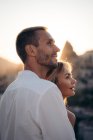 Seitenansicht eines verliebten Mannes und einer verliebten Frau, die zusammen auf der Straße stehen und gegen den Sonnenuntergang wegschauen — Stockfoto