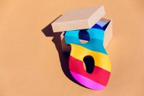 Maschera multicolore mascherata per evento festivo collocata in scatola di cartone aperta con coperchio su sfondo arancione in leggero studio moderno — Foto stock