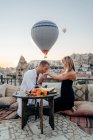 Uomo baciare la mano della fidanzata mentre seduto sul tetto in città con mongolfiere che volano nel cielo serale — Foto stock