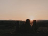 Couple de hippies avec des lunettes de soleil couché sur une prairie herbeuse dans la nature tout en regardant le coucher du soleil dans les montagnes — Photo de stock