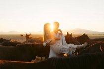 Мужчина, держащий светловолосую девушку среди лошадей на сельском пастбище, глядя друг на друга — стоковое фото