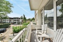 Moderno edificio residenziale con poltrone e tavolo su balcone recintato con piante in vaso sotto cielo blu nuvoloso ad Amsterdam — Foto stock