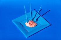 Heap de cérebros crus rosa servido em placa azul com garfos de plástico no fundo azul no estúdio criativo moderno claro — Fotografia de Stock