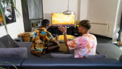 Dall'alto vista posteriore di anonimi amici maschi multirazziali seduti sul divano con gamepad in mano che giocano a videogame in soggiorno — Foto stock