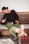 Веселая молодая этническая женщина ласкает милую кошечку, делая автопортрет на скамейке — стоковое фото