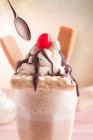 Cuillère atteignant à milkshake sucré appétissant décoré de crème fouettée et gaufres et cerise sur le dessus — Photo de stock