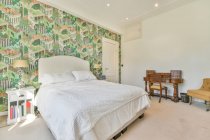 Interior do quarto espaçoso com cama macia confortável e mobiliário de madeira estilo clássico e poltrona em apartamento leve — Fotografia de Stock