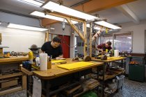 Artesãos focados luthiers trabalhando na própria oficina de reparação de guitarras elétricas com diferentes equipamentos profissionais e paredes de vidro — Fotografia de Stock