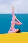 Corpo pieno di donna magra in activewear facendo esercizio su tappetino giallo contro parete blu — Foto stock
