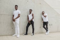 Повне тіло крутих афроамериканських чоловіків у модному одязі з білою футболкою, що стоїть біля будівлі і дивиться на камеру. — стокове фото