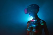 Матуся жінки в футуристичних окулярах VR, розміщених під яскравою проекцією в тьмяній кімнаті — стокове фото