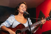 Fiduciosa signora con chitarra che canta in microfono durante l'esecuzione di una canzone in un club luminoso — Foto stock