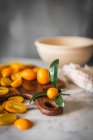 Mucchio di kumquat freschi tagliati all'arancia su tagliere di legno posto sul tavolo di marmo con asciugamano in cucina — Foto stock