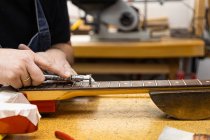 Crop anonymous master polishing frets on guitar neck with professional polishing wheel at table in light workshop on blurred background — Stock Photo