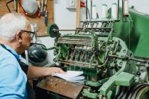 Crop faceless trabalhador masculino de meia idade colocando pilha de papéis em máquina de corte de metal envelhecido na fábrica — Fotografia de Stock