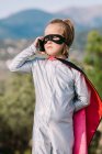 Menina auto-assegurada no traje de super-herói máscara olho com capa ter telefonema no celular — Fotografia de Stock
