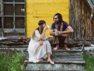 Hippie hombre viendo una hermosa mujer hippie beber de una taza en un porche de madera - foto de stock