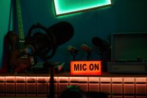 Micrófono moderno en trípode colocado en la mesa en estudio oscuro con iluminación de neón antes de grabar podcast - foto de stock