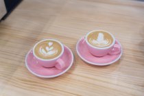 Кружки горячего кофе с креативным латте на тарелке с чайной ложкой на деревянном столе в современном светлом кофейне — стоковое фото