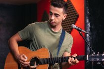 Молодой гитарист играет на акустической гитаре и поет в микрофон в лайт-клубе — стоковое фото