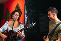 Позитивний молодий чоловік грає на гітарі біля жіночого музиканта, грає на акустичній гітарі та співає у легкому клубі — стокове фото