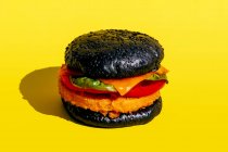 From above fresh burger with black bun and vegetables on yellow background — Stock Photo