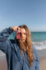 Молода жінка в мокрому одязі фотографується на камеру, стоячи, дивлячись на камеру на піщаному пляжі біля махаючого моря — стокове фото