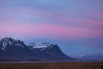 Paisagem pitoresca de montanhas rochosas com picos nevados perto do mar contra o incrível céu de pôr-do-sol rosa na Islândia — Fotografia de Stock