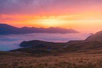 Colina pastosa perto de névoa branca grossa contra cume de montanha contra o céu colorido do pôr-do-sol na natureza selvagem da Espanha em Pirinéus — Fotografia de Stock