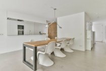 Modernes Esszimmer und Küche mit eingebauten Elektrogeräten gegen Tisch mit Stühlen im Haus — Stockfoto