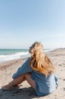 Unerkennbare Frau im Hemd sitzt am Sandstrand am Meer und genießt den Sommertag — Stockfoto
