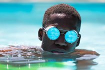 Спокійний афроамериканець у стильних сонцезахисних окулярах із зображенням води, що плаває в басейні на тлі розмитого фону в сонячний літній день. — стокове фото