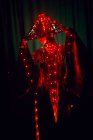 Femme énigmatique méconnaissable en tenue traditionnelle créative et coiffures vietnamiennes avec éclairage rouge debout en studio sombre sur fond noir pendant la performance — Photo de stock