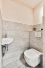 Interior do banheiro contemporâneo com vaso sanitário e lavatório na parede de azulejos cinza na casa de luz — Fotografia de Stock
