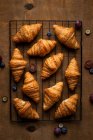 Von oben leckere süße frisch gebackene Croissants serviert mit Früchten auf Metallrost auf dem Holztisch — Stockfoto