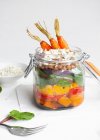 Салат с разноцветным спелым перцем и булгуром, увенчанным сырой морковью, подаваемой в банке на белом фоне — стоковое фото