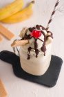 De cima de frasco de vidro de banana doce split milkshake coberto com chantilly waffles chocolate e cereja na placa de corte — Fotografia de Stock