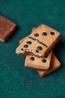 Un mucchio di dolci gustosi biscotti croccanti a forma di domino con punti neri e pezzo morso sparsi sulla superficie verde nella stanza della luce — Foto stock