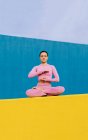 Спокійна, гнучка жінка сидить у Падмасані і медитує закритими очима, практикуючи йогу на яскравому синьому і жовтому фоні. — стокове фото