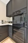 Design criativo de cozinha com forno elétrico e microondas contra armários e mesa em casa — Fotografia de Stock