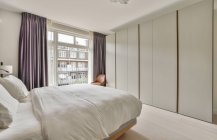 Комфортне ліжко і мінімалістичний стиль шафи, розташованої біля вікна з шторами в сучасній спальні — стокове фото
